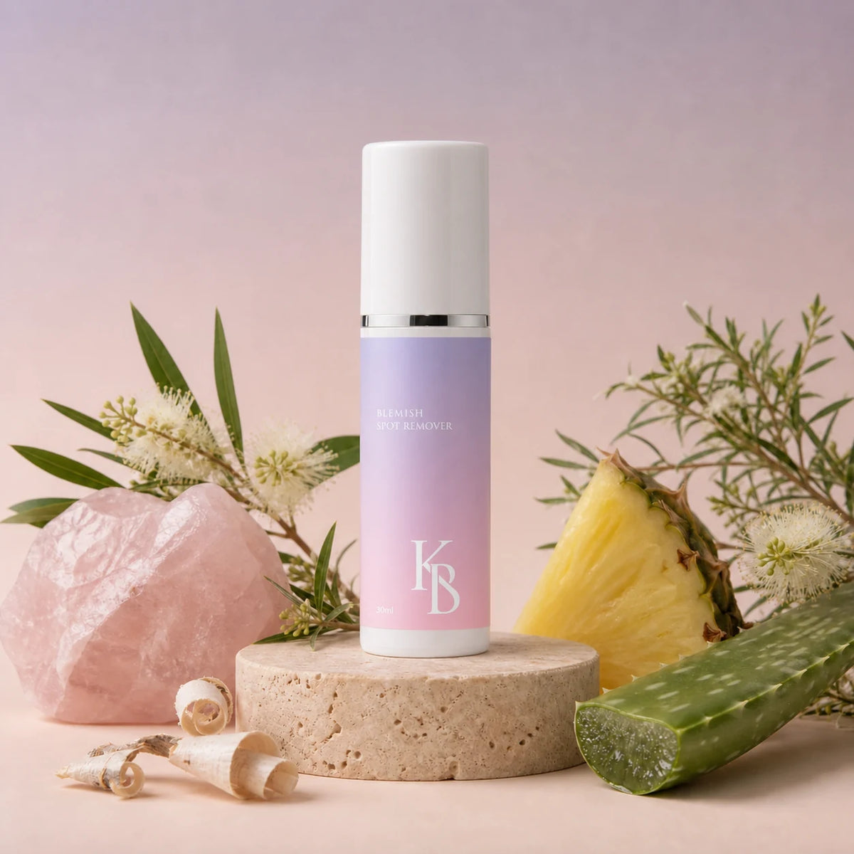Kaloneo Beauty Blemish Spot Remover 30ml on a travertine plinth with rose quartz, tea tree blossom, pineapple, aloe vera and curls of white willow bark, the botanicals used in the formula