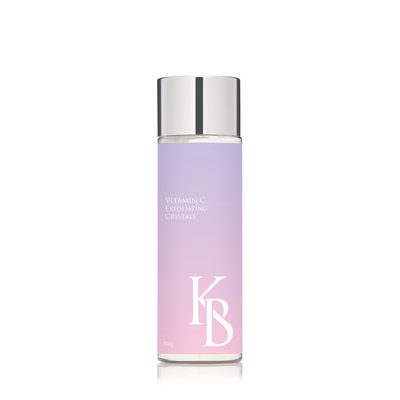 A bottle of Vitamin C Exfoliating Crystals with a purple to clear gradient and the brand's logo 'KB' on the label.