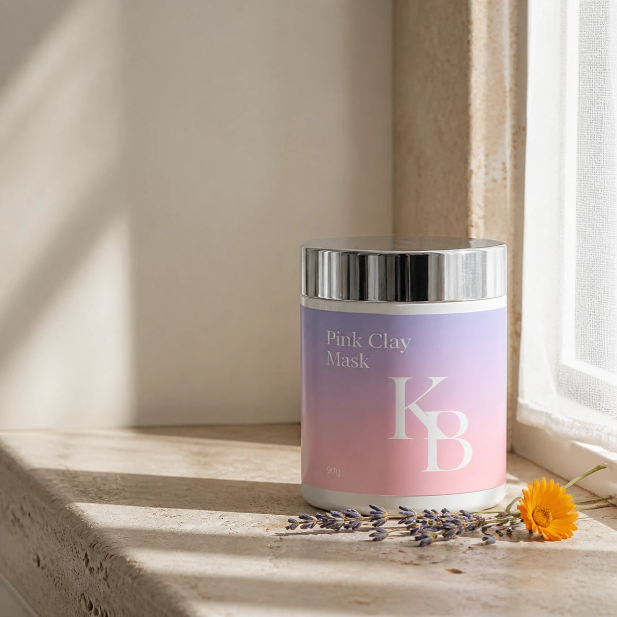Kaloneo Beauty Pink Clay Mask 90g jar standing on a travertine window ledge in morning light, dried lavender and a calendula flower beside it
