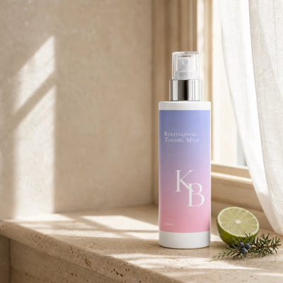 Kaloneo Beauty Revitalising Toning Mist 125ml standing on a travertine ledge in morning light, a sheer curtain behind and a halved lime and juniper sprig beside it