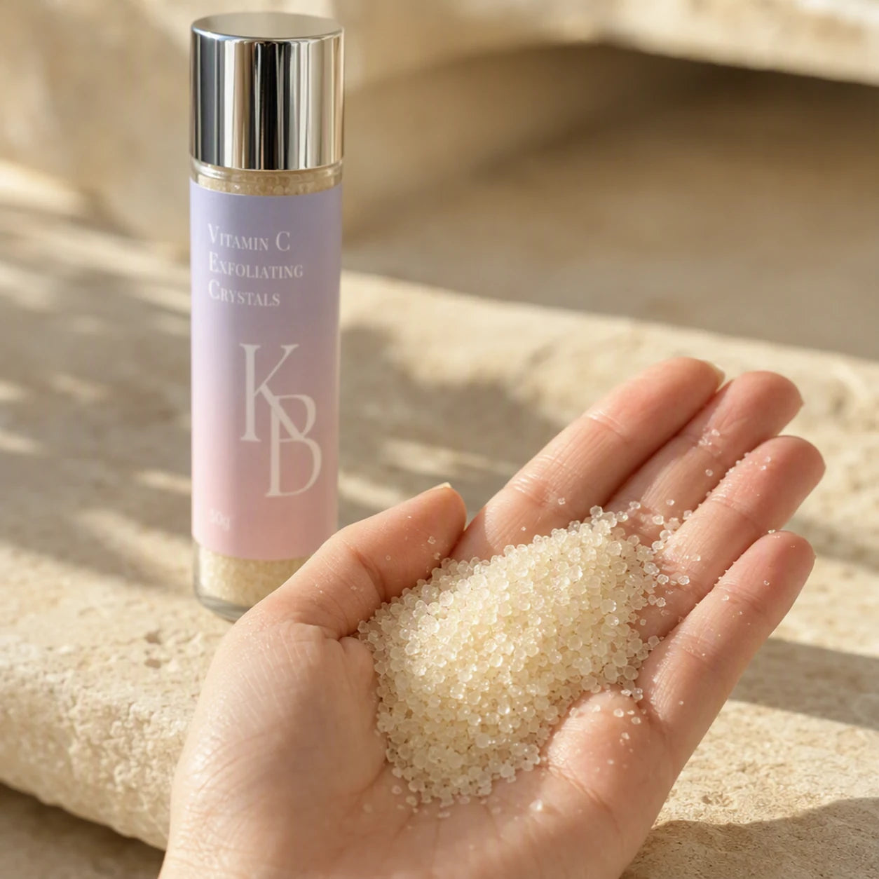 Close-up of Kaloneo Beauty Vitamin C Exfoliating Crystals in an open palm, a coarse off-white exfoliating powder