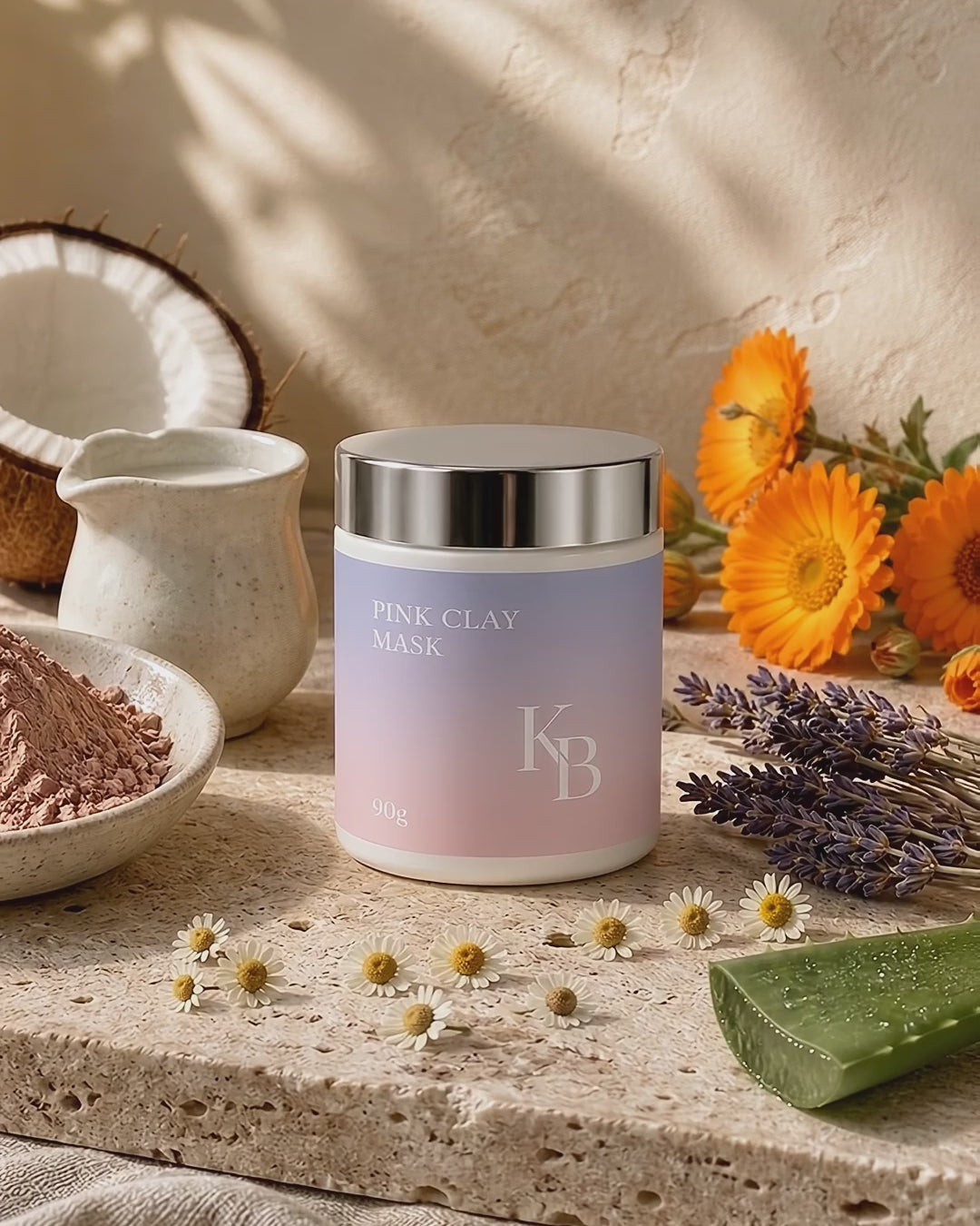 Load video: Kaloneo Beauty Pink Clay Mask on travertine surrounded by raw pink clay, coconut, calendula, chamomile, lavender and aloe vera in soft daylight - portrait product film with music